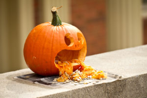 A carved pumpkin with seeds vomiting from its mouth
