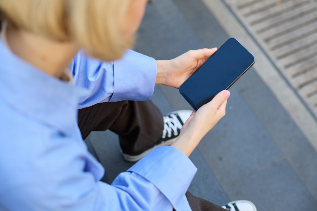 Young person using smartphone outdoors, showing the rise of online booking for Gen Z over traditional calls.