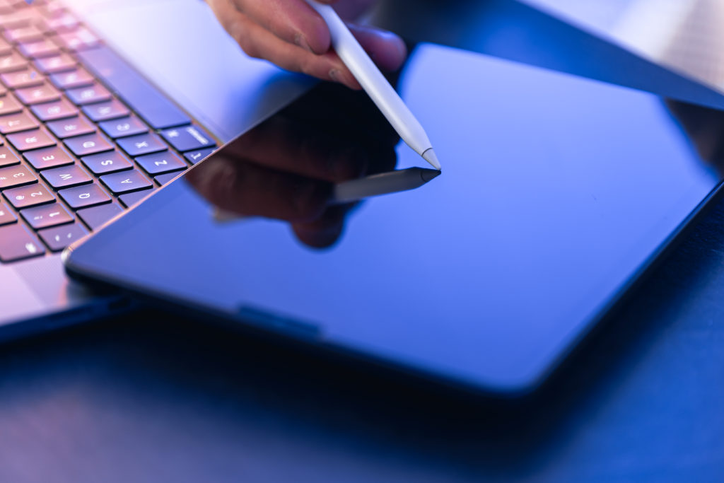 Hand using stylus on tablet beside laptop, representing a paperless booking system and green business scheduling.