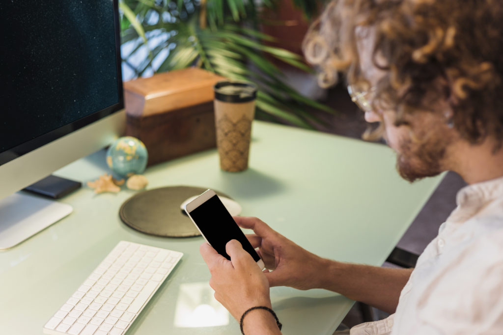 Curly-haired person at desk using smartphone, showing SimplyBook.me client app and client's booking habits.