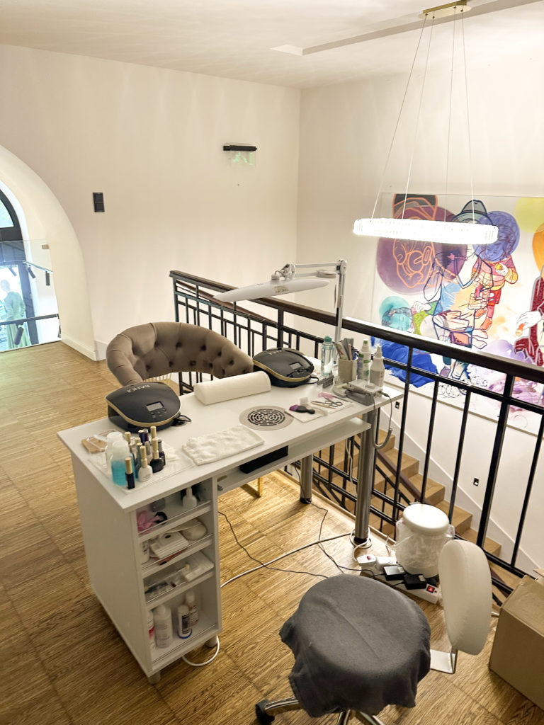 Cozy nail salon station with wooden floors, a tufted chair, and various nail products. A colorful abstract painting hangs on the wall, adding vibrancy.