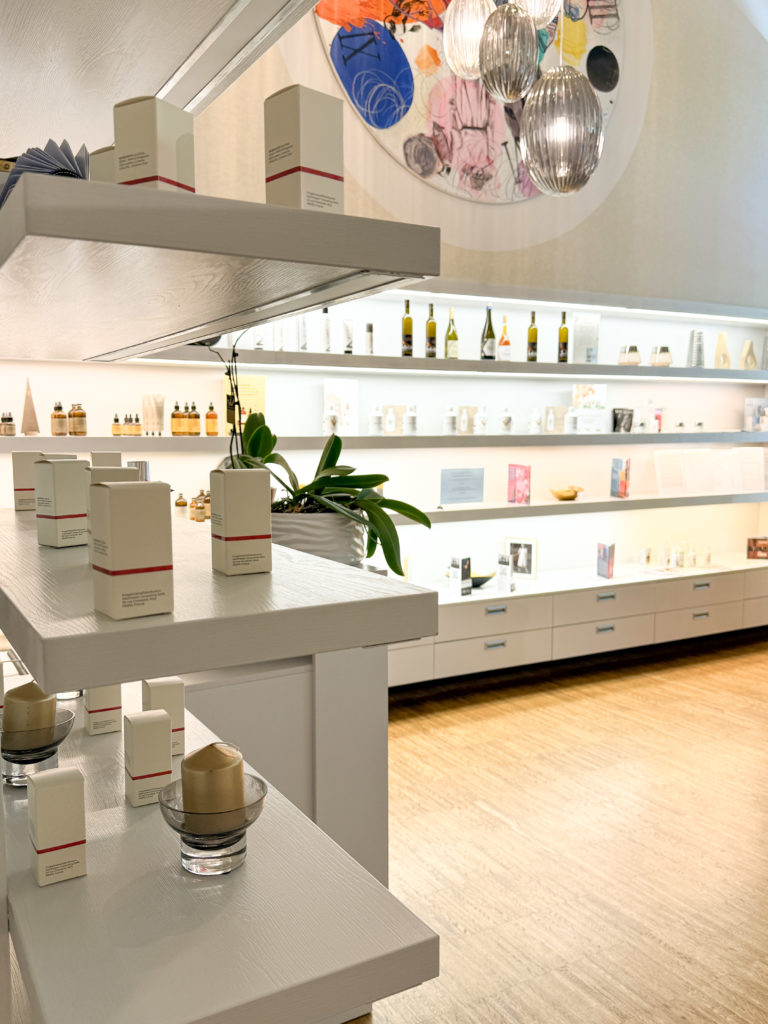 Modern store interior with white shelves displaying skincare products and bottles, under soft lighting. An abstract circular artwork hangs above.