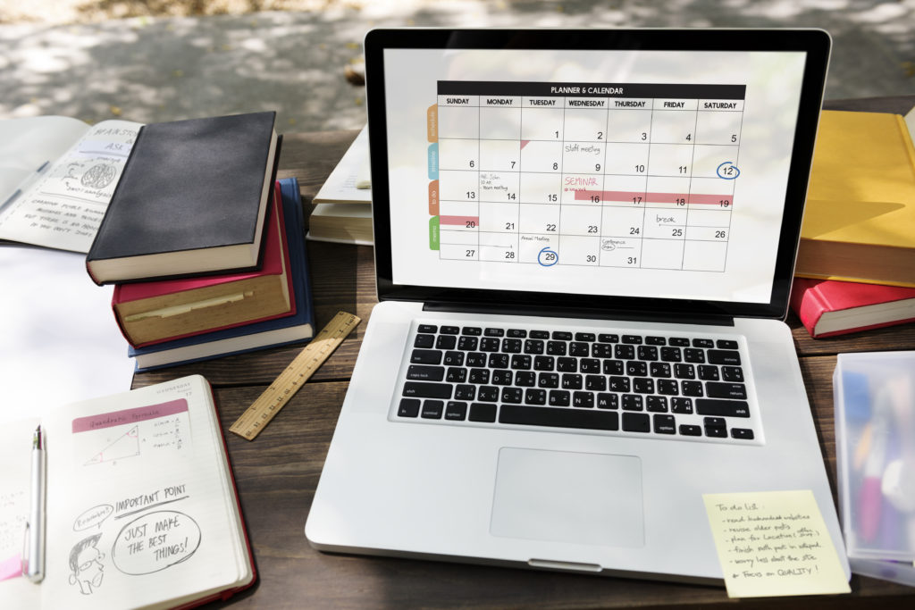 Open laptop showing a digital calendar on a wooden desk surrounded by books, notes, and a ruler, reflecting an organized school workspace.