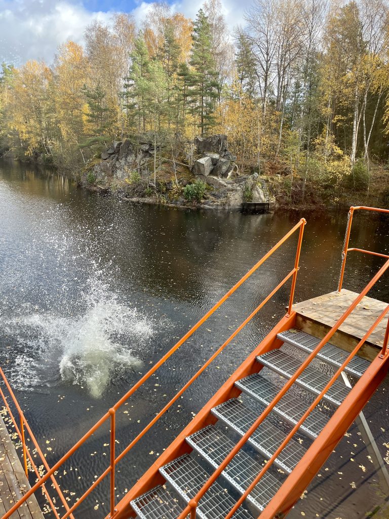 Orangefarbene Metalltreppen führen hinunter zu einem See mit einer großen Wasserfläche, die einen kürzlichen Tauchgang zeigt.  