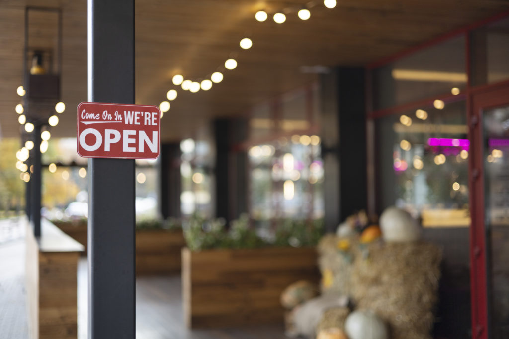 Outdoor business decorated with festive lights and pumpkins on hay bales, featuring a red ‘We’re Open’ sign — representing a multi-location business welcoming customers.
