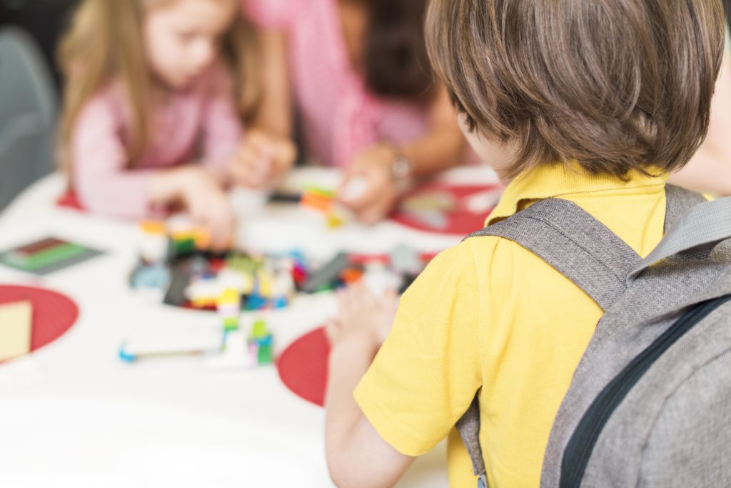 Young student with backpack building colorful blocks in a classroom, illustrating hands-on learning and collaborative school activities.