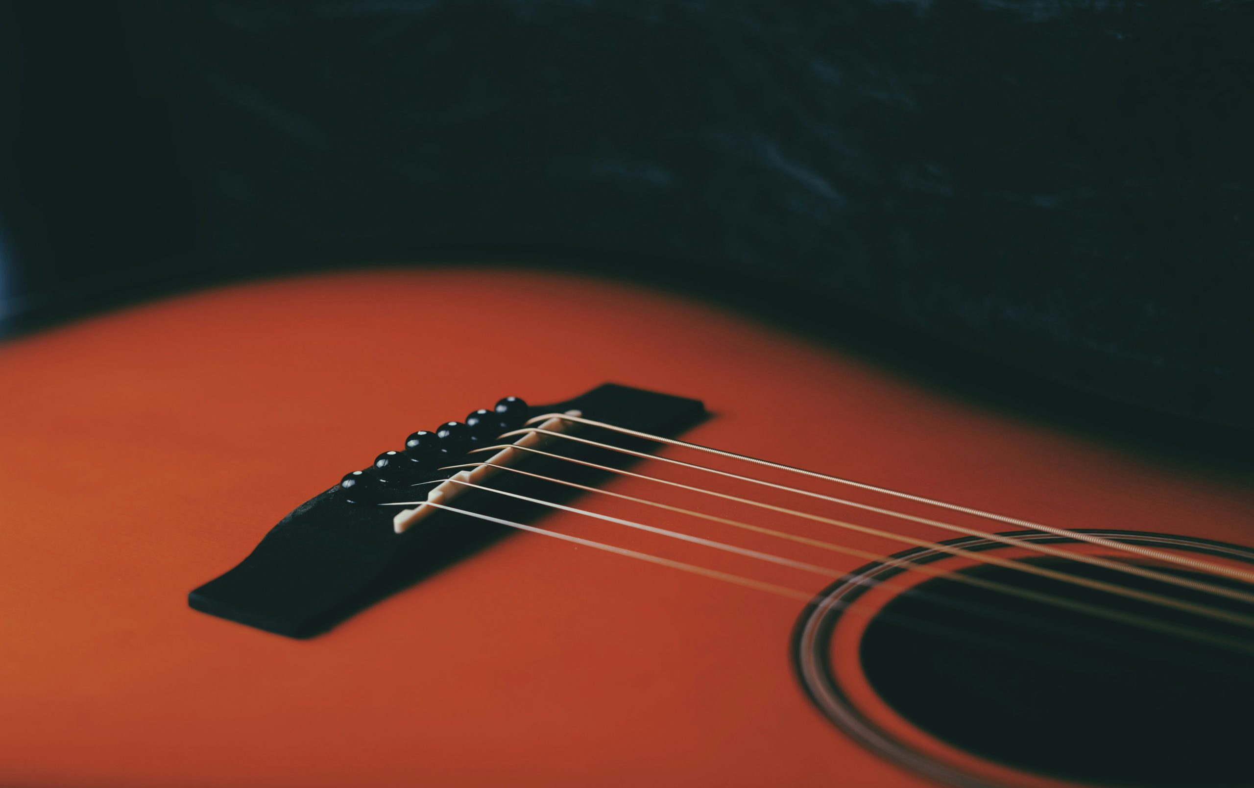Close-up of an acoustic guitar's strings and bridge on a warm, orange-toned body. 
