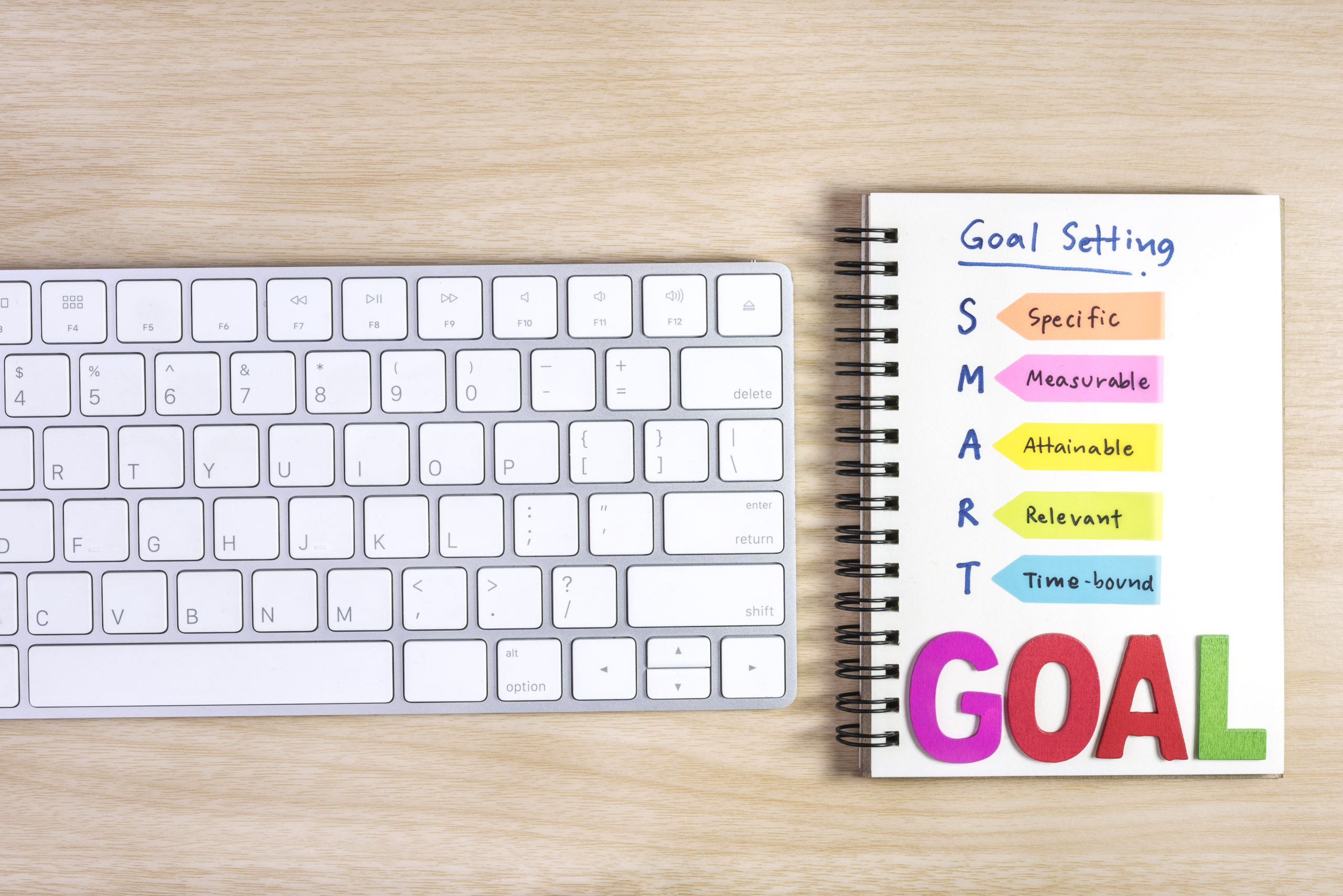 White keyboard beside a notebook titled “Goal Setting” with colorful SMART goal bars, representing booking automation for business growth planning.